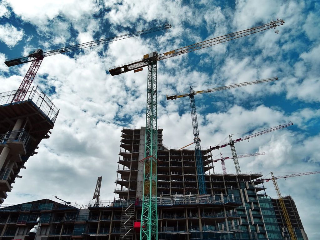 green-and-yellow-crane-439416 Urban construction site with numerous cranes framing rising skyscrapers against a blue sky.